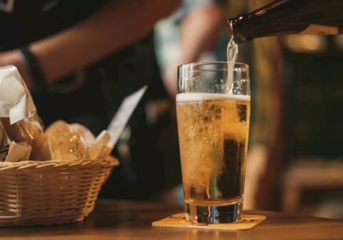 A bartender pours beer into a tall glass beside a basket of fries in a cozy bar.