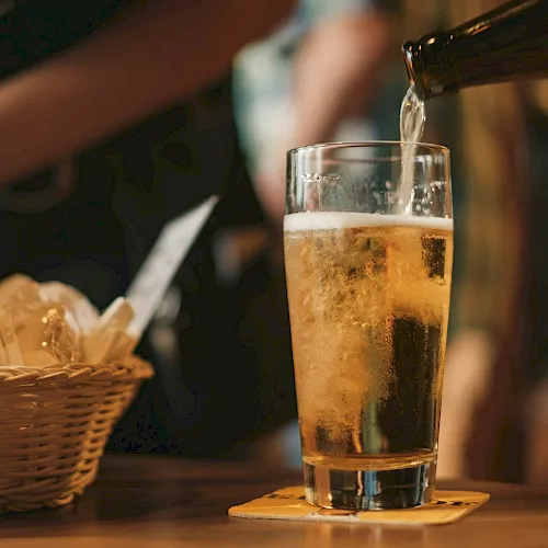 A bartender pours beer into a tall glass beside a basket of fries in a cozy bar.