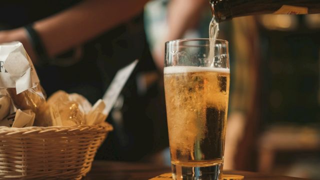 A bartender pours beer into a tall glass beside a basket of fries in a cozy bar.