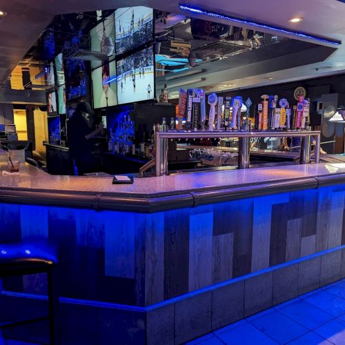 A modern bar interior with blue lighting, pool tables, a snack counter, and taps behind the bar.